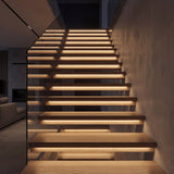 Luces LED integradas en cada peldaño de una escalera flotante de madera en vivienda de lujo.