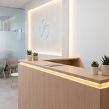 Luz LED lineal perimetral integrada en un mueble de recepción de madera para arquitectura comercial.