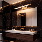 Aplique Nerina Old Brass sobre espejo en baño con revestimiento de mármol negro.
