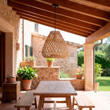 Lámpara de rattan natural en mesa de picnic bajo techo de vigas de madera a la vista.