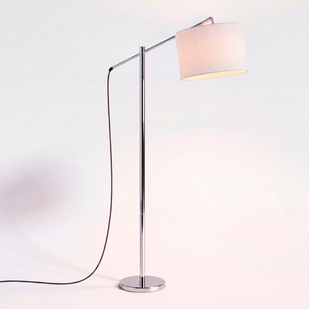 Luminaria esbelta con brazo extensible cromado y pantalla de tela blanca para una distribución lumínica limpia.