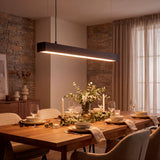 Luminaria lineal suspendida emitiendo luz cálida sobre mesa de madera en salón elegante.