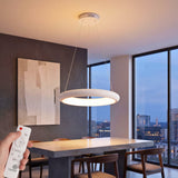 Luminaria circular LED blanca suspendida sobre mesa de comedor de diseño con control remoto manual.
