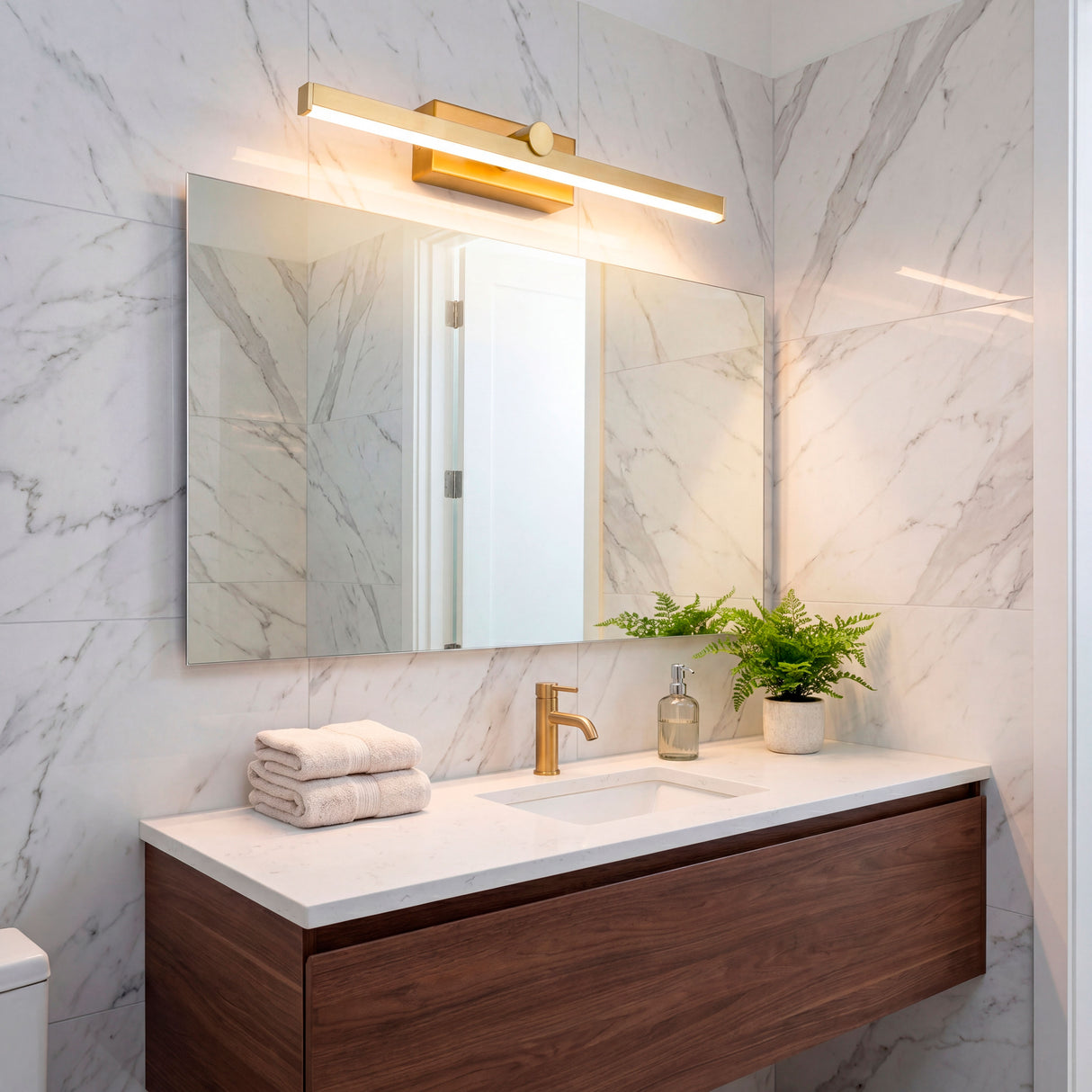 Aplique LED dorado sobre espejo rectangular en baño con revestimiento de mármol.