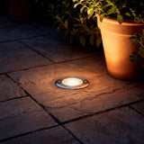 Luminaria empotrable de suelo proyectando luz cálida sobre pavimento de piedra en arquitectura contemporánea.