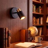 Spot articulado en negro y dorado que aporta un baño de luz cálida sobre escritorio de madera de roble.