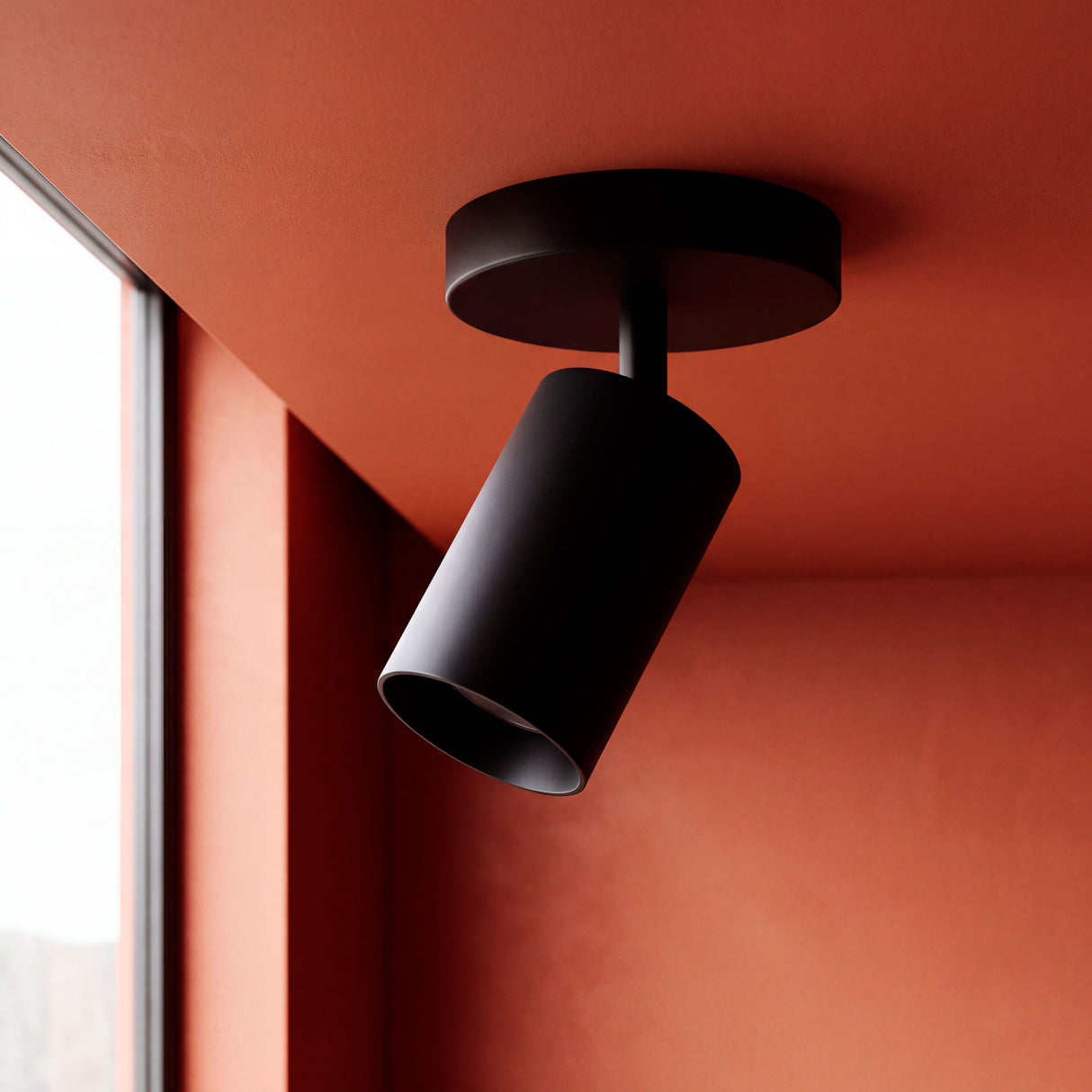 Spot técnico orientable en negro mate instalado sobre techo terracota de arquitectura contemporánea.
