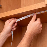 Manos técnicas aplicando presión para fijar una línea lumínica flexible en el interior de un mueble.