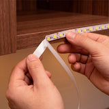 Manos técnicas aplicando presión para fijar una línea luminosa flexible en el interior de una repisa.