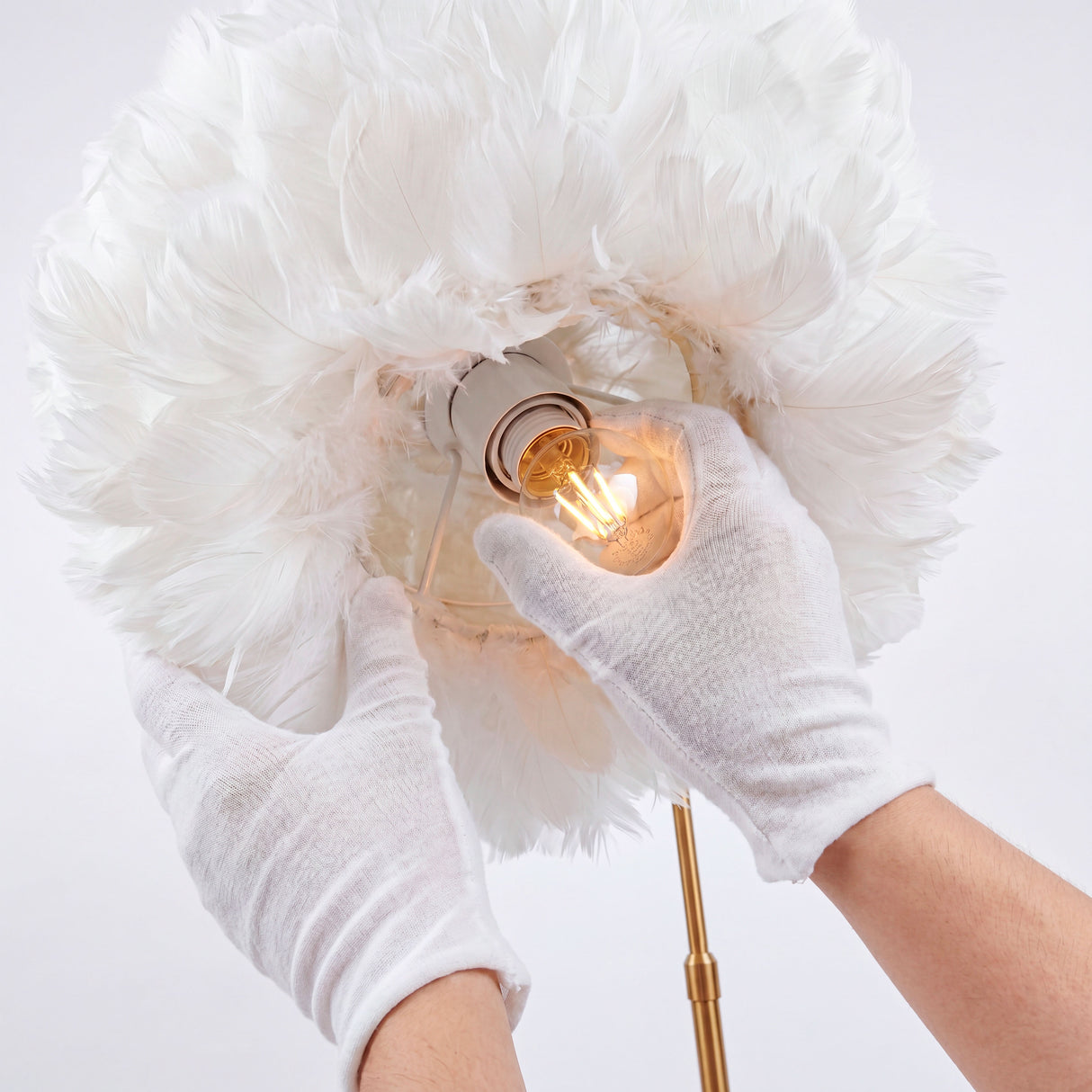 Manos técnicas con guantes blancos instalando una bombilla en el interior de la pantalla de plumas.