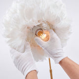 Manos técnicas con guantes blancos instalando una bombilla en el interior de la pantalla de plumas.