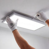 Especialista instalando panel LED rectangular blanco con guantes de protección.