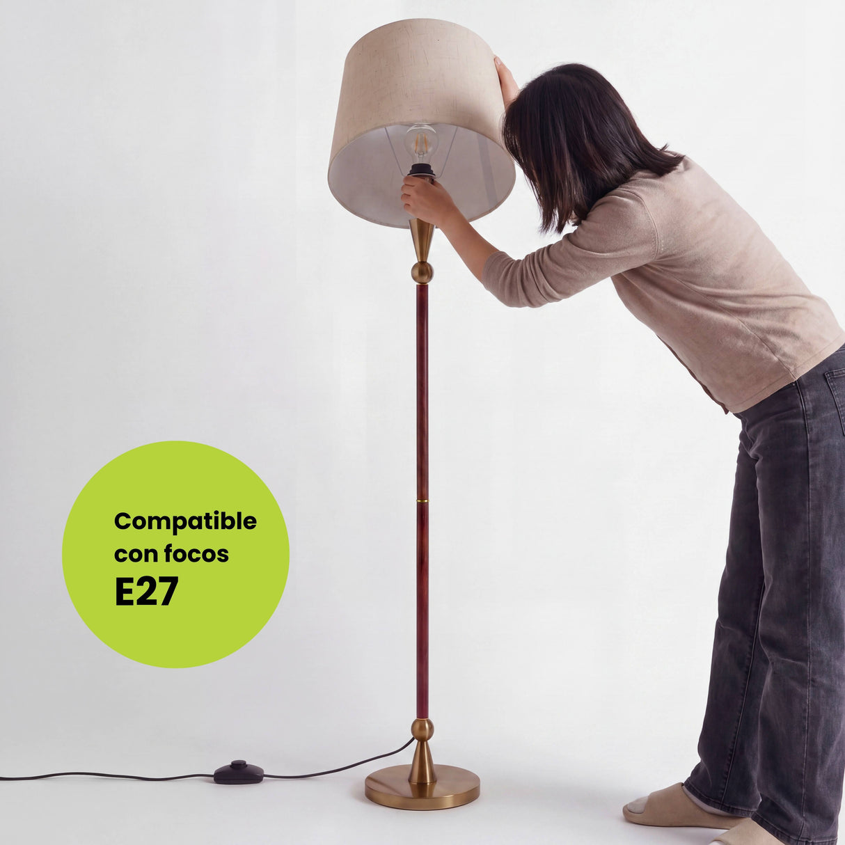 Mujer ajustando pantalla cilíndrica beige en socket E27 compatible con lámparas de eficiencia lumínica.