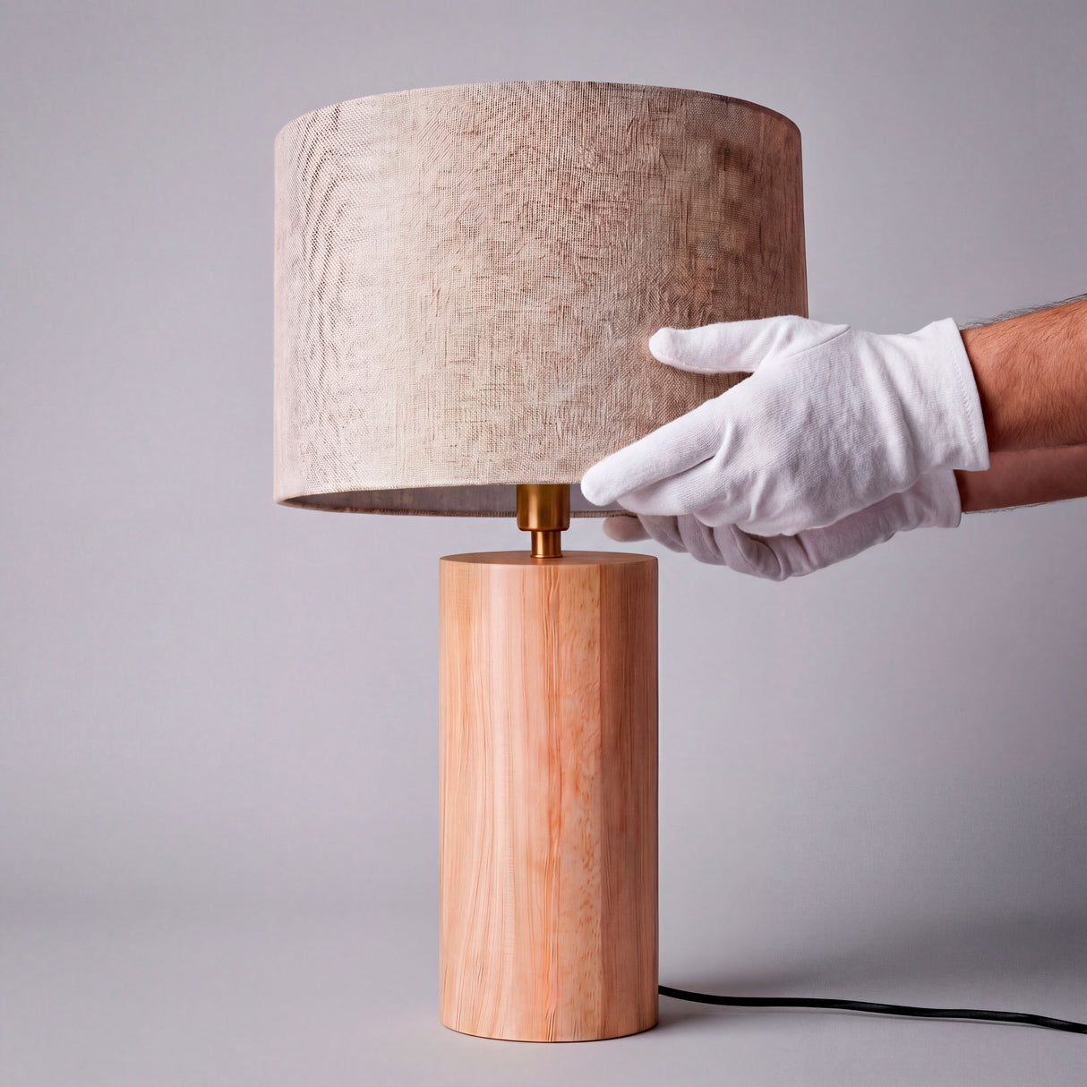 Detalle del montaje de pantalla beige sobre base cilíndrica de madera con guantes técnicos.