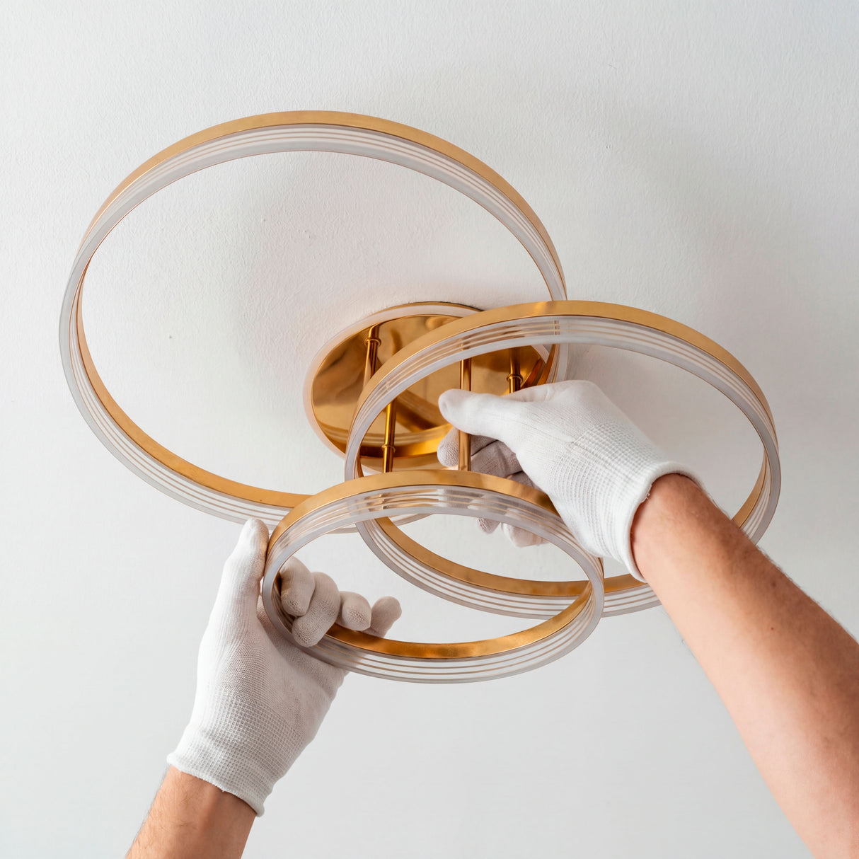Especialista ajustando los aros de la luminaria dorada utilizando guantes de microfibra.