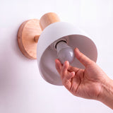 Proceso de colocación de bombilla E27 en luminaria orientable de pared con pantalla blanca.