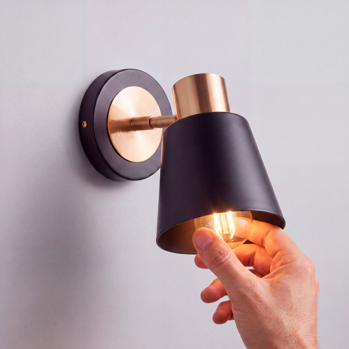 Proceso de colocación de bombilla E27 en luminaria orientable de pared con pantalla negra.