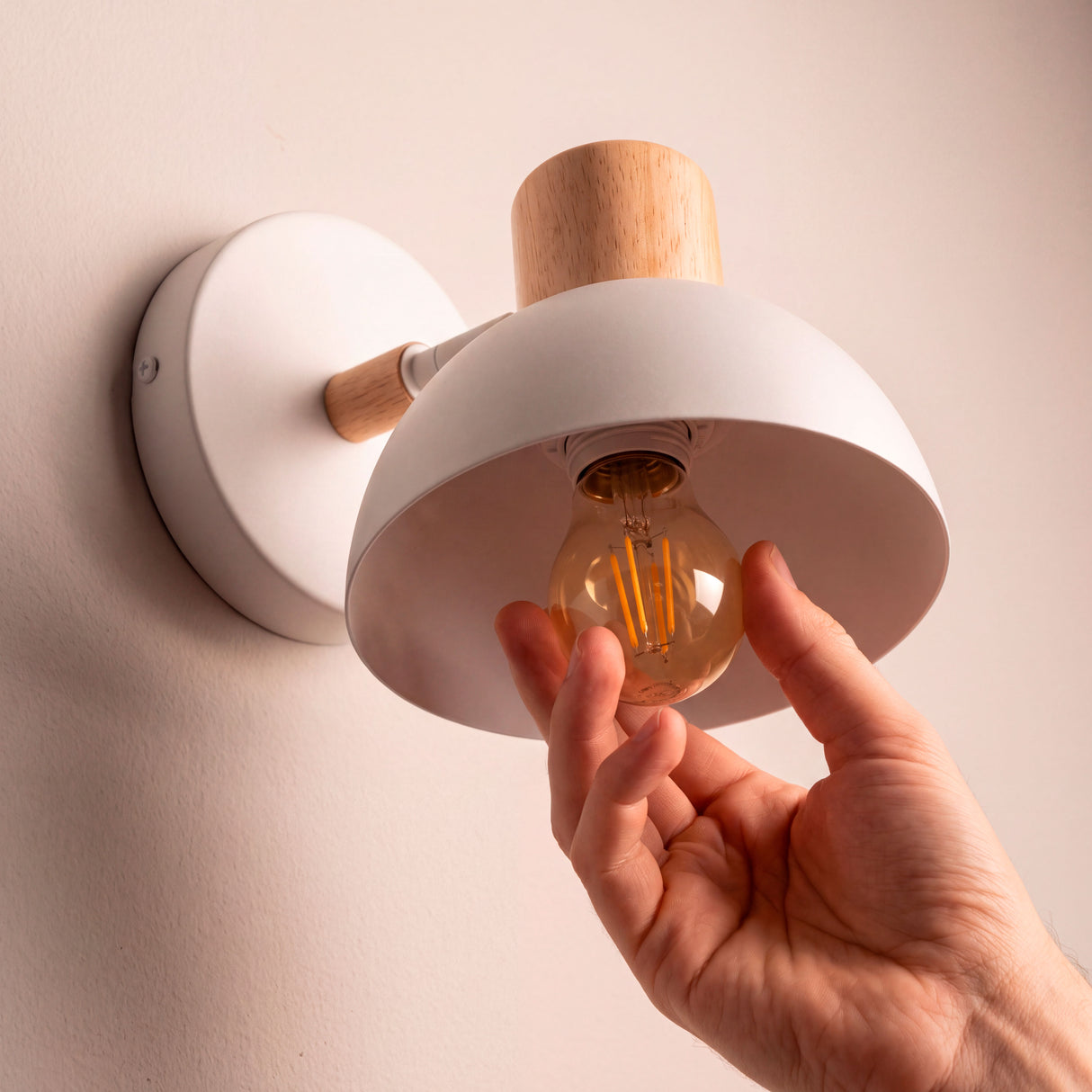 Proceso de colocación de bombilla E27 en luminaria orientable de pared con pantalla blanca.