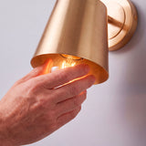 Proceso de colocación de bombilla E27 en luminaria orientable de pared en dorado cepillado.