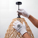 Ajuste de florón negro mate en luminaria de mimbre utilizando guantes de protección técnica.