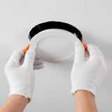 Proceso de colocación de luminaria circular en techo con guantes de protección técnica.