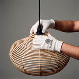 Ajuste del cable de suspensión y porta lámparas en campana de rattan con guantes de protección.