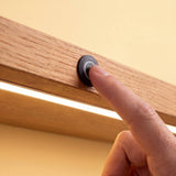 Dedo tocando interruptor sensor táctil que enciende cinta LED en repisa de madera