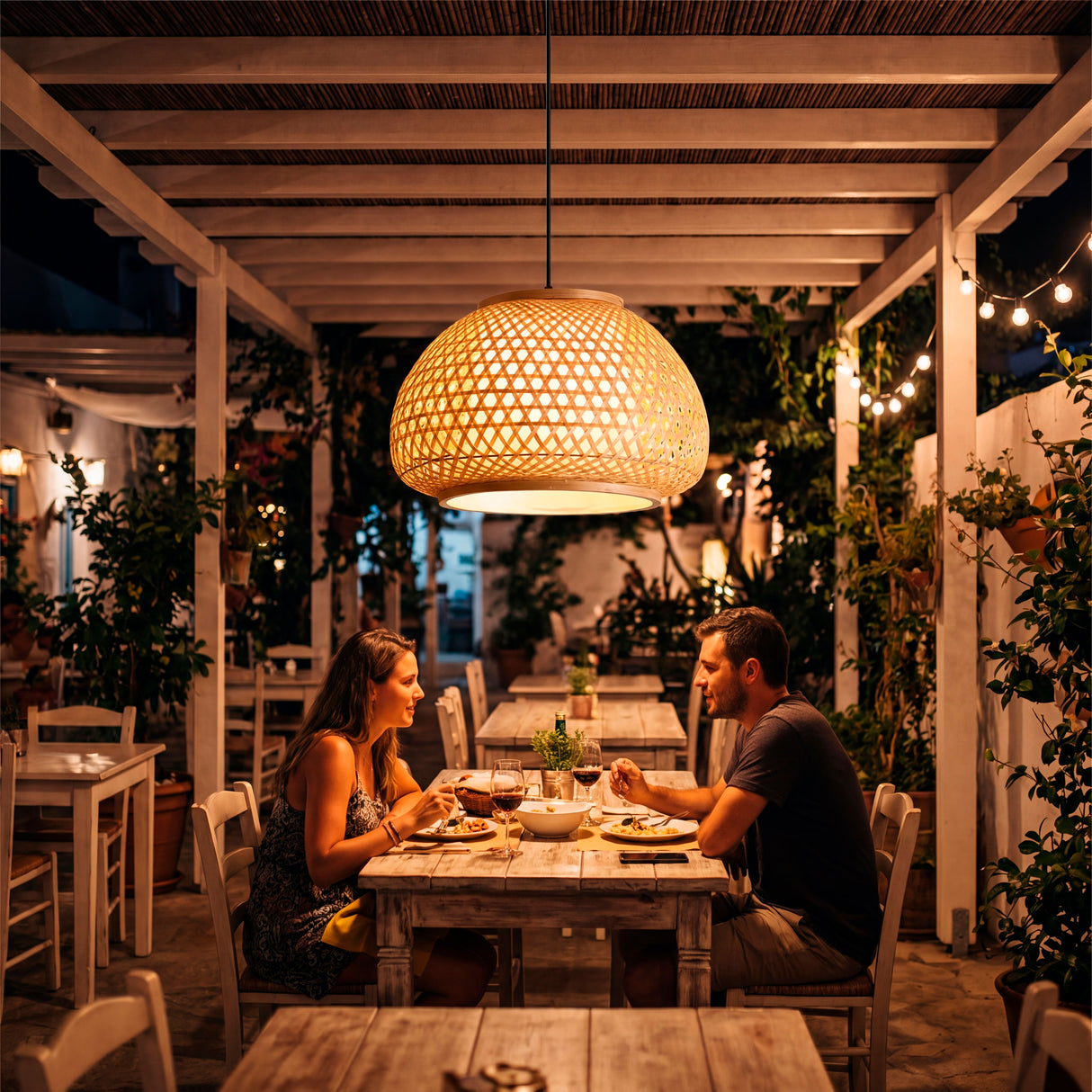 Mesa de restaurante al aire libre iluminada por el resplandor de la lámpara Belinda de noche.