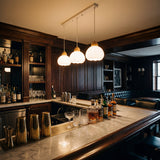 Iluminación decorativa lineal sobre barra de bar con acabados en madera oscura.