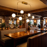 Lampara de techo lineal dorada con esferas blancas en salon de restaurante rustico moderno.