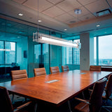 Lámpara colgante lineal LED Frida Clear sobre mesa de directorio ejecutiva de madera.