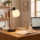 Lámpara de escritorio negra iluminando mesa de trabajo con decoración cálida