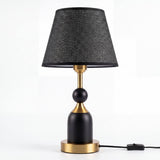 Lámpara de mesa ALBA BLACK AND GOLD apagada con cable e interruptor sobre fondo claro