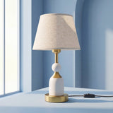 Lámpara de mesa blanca con detalles dorados sobre mesa junto a la ventana
