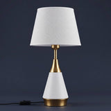 Lámpara de mesa AMIRA WHITE AND GOLD encendida sobre fondo azul oscuro elegante