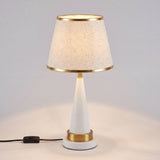Lámpara de mesa AURELIA WHITE AND GOLD con pantalla de ribetes dorados sobre fondo crema