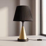 Lámpara de mesa con cono de latón y pantalla plisada negra junto a la ventana