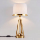 Lámpara de mesa dorada encendida con su pantalla blanca brillando cálida