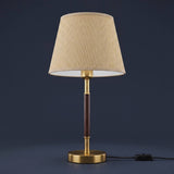 Lámpara de mesa MARGOT WALNUT AND GOLD encendida sobre fondo azul oscuro elegante