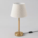 Lámpara de mesa MARGOT WOOD AND GOLD dorada y madera clara sobre fondo gris neutro