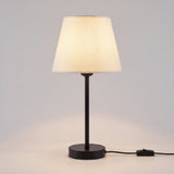 Lámpara de mesa NORA encendida con luz cálida sobre fondo neutro
