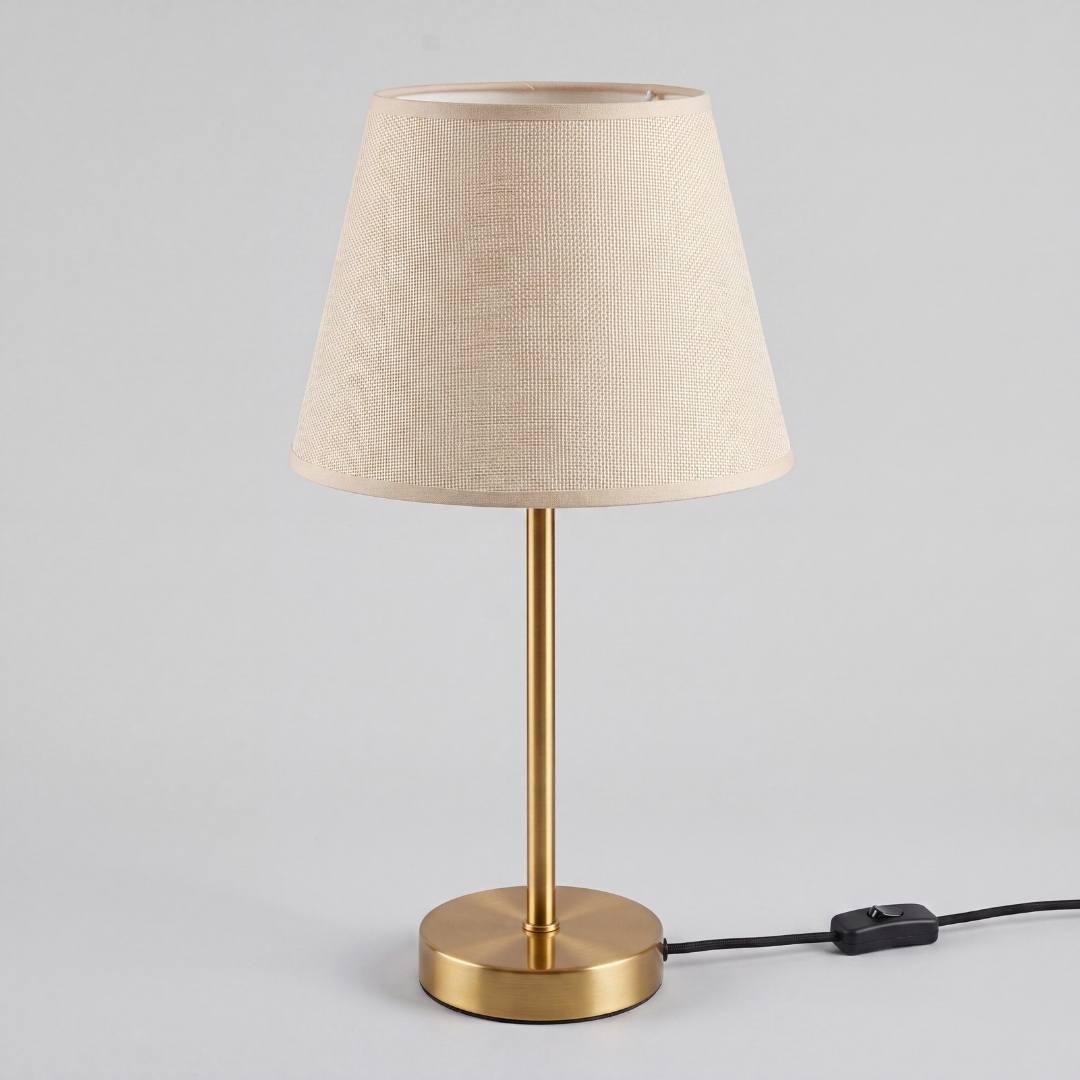 Lámpara de mesa NORA GOLD encendida con luz cálida y cable con interruptor visible
