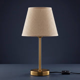 Lámpara de mesa NORA GOLD dorada apagada sobre fondo azul grisáceo elegante