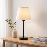 Lámpara de mesa NORA junto a planta sobre mesa auxiliar de madera