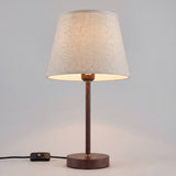 Lámpara de mesa NORA WALNUT encendida mostrando su pantalla de lino con luz cálida