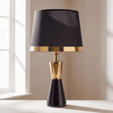 Lámpara de mesa CLEO GOLD negra con aro dorado junto a ventana luminosa