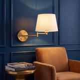 Lámpara de pared articulable GALA Gold encendida junto a butaca en muro azul