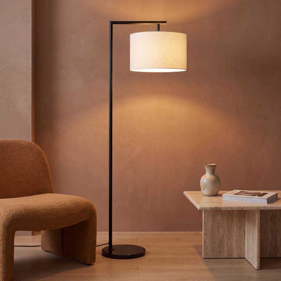 Lámpara de pie MARA BLACK con base de mármol encendida junto a butaca terracota