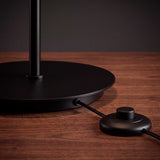 Interruptor de pie negro sobre piso de madera junto a la base de la lámpara