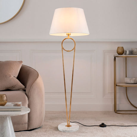 Lámpara de pie Olinda Gold con base de mármol y pantalla blanca en salón lujoso.